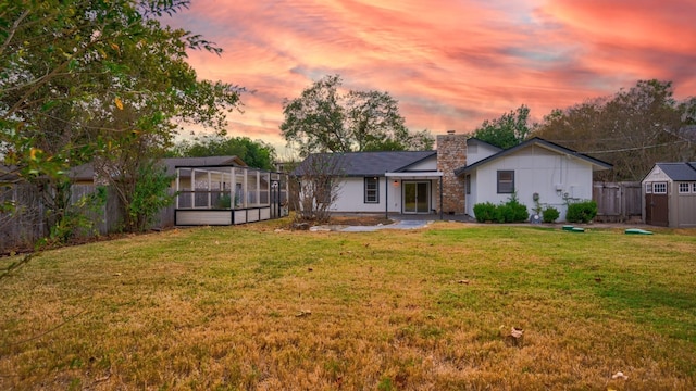 back house at dusk featuring a lawn and glass enclosure