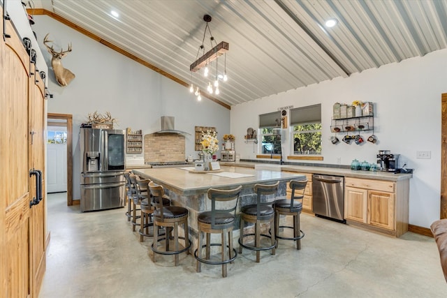 kitchen with a center island, wall chimney exhaust hood, stainless steel appliances, hanging light fixtures, and a barn door