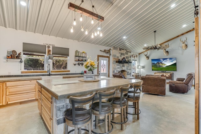 kitchen with light brown cabinets, a kitchen breakfast bar, hanging light fixtures, high vaulted ceiling, and a center island