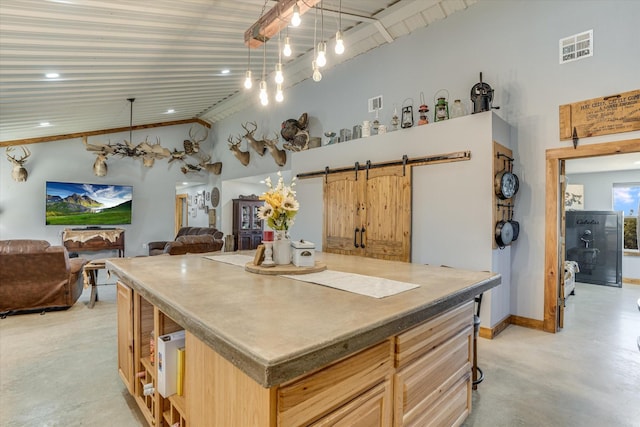 kitchen with a barn door, a kitchen island, hanging light fixtures, light brown cabinets, and high vaulted ceiling