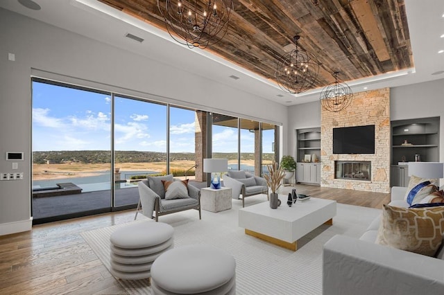 living room featuring a fireplace, built in features, a notable chandelier, a tray ceiling, and light hardwood / wood-style flooring