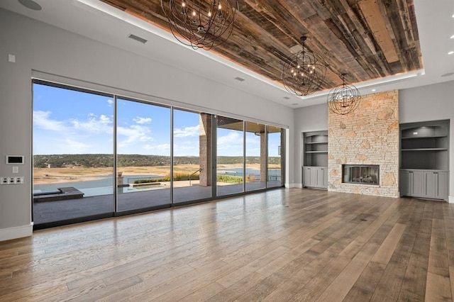 unfurnished living room with a notable chandelier, hardwood / wood-style floors, a raised ceiling, built in features, and a stone fireplace