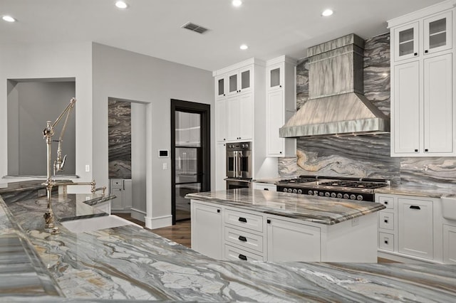 kitchen featuring light stone countertops, white cabinets, and custom range hood