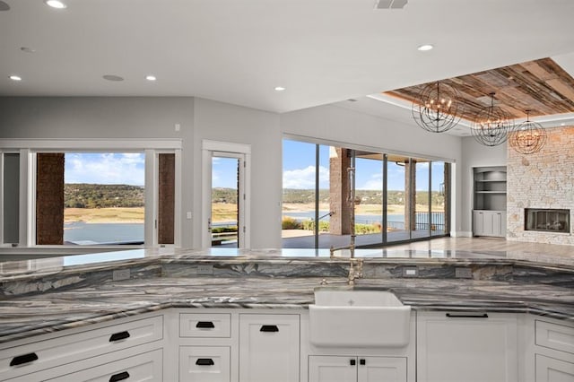 kitchen featuring built in shelves, a notable chandelier, a stone fireplace, and white cabinetry