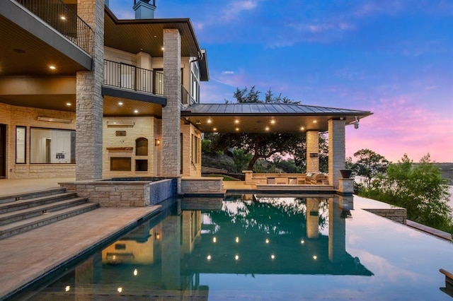 pool at dusk featuring a patio area, an outdoor stone fireplace, and a gazebo