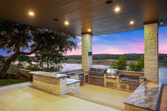 patio terrace at dusk with an outdoor kitchen, a water view, area for grilling, and sink