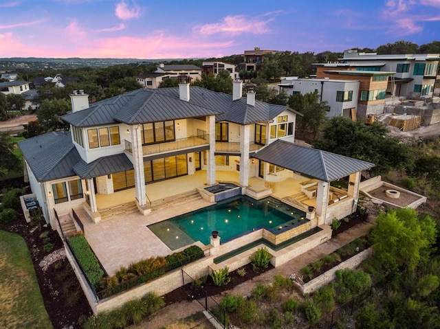 back house at dusk with a swimming pool with hot tub and a patio