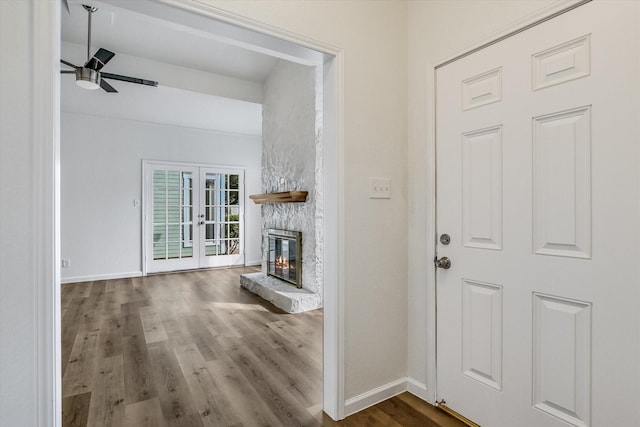 unfurnished living room featuring french doors, ceiling fan, hardwood / wood-style floors, and a stone fireplace