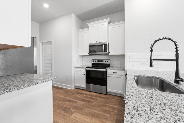 kitchen with light stone countertops, white cabinets, appliances with stainless steel finishes, sink, and dark hardwood / wood-style floors