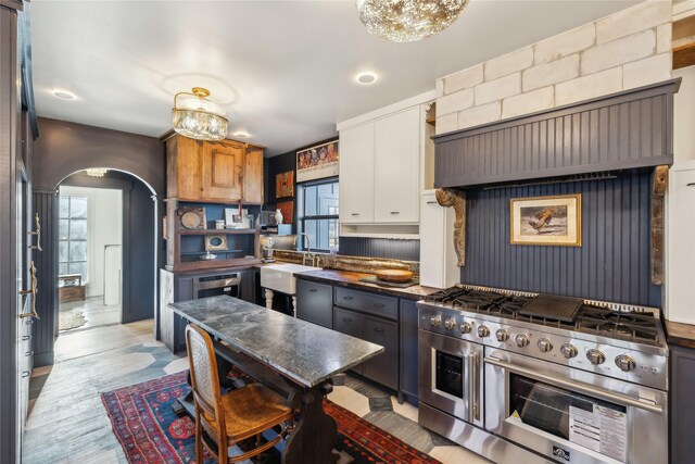 kitchen featuring high end stainless steel range oven, light wood-type flooring, and sink