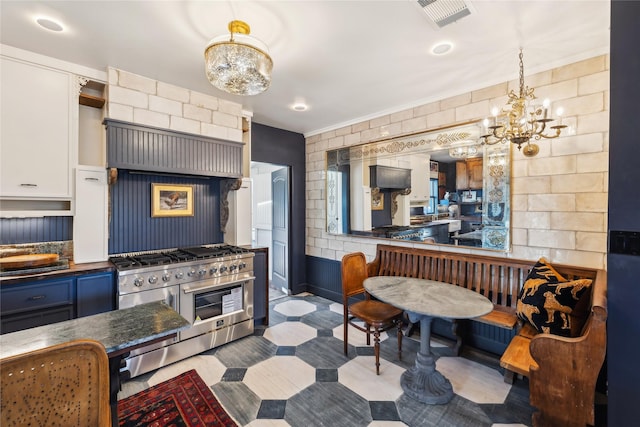 kitchen with pendant lighting, range with two ovens, white cabinetry, and a chandelier