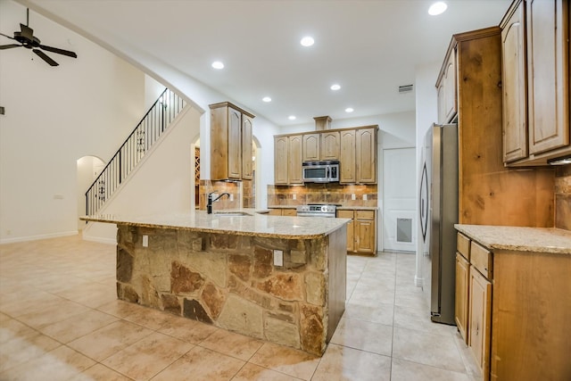 kitchen with backsplash, kitchen peninsula, sink, appliances with stainless steel finishes, and light stone counters