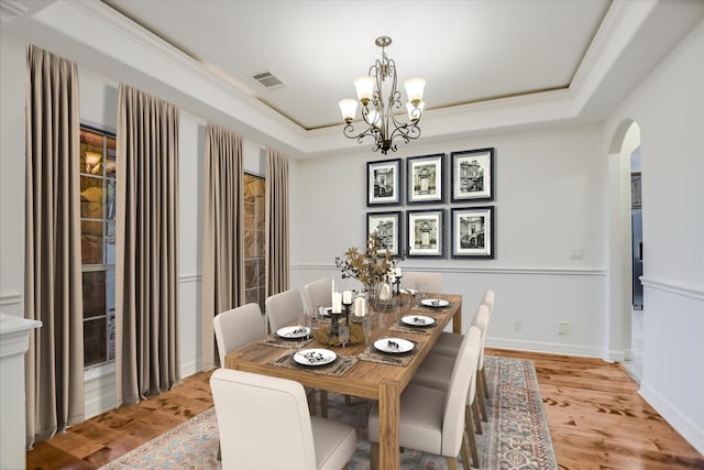 dining area with crown molding, light wood-type flooring, a tray ceiling, and a chandelier