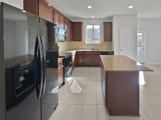 kitchen featuring a center island, black appliances, sink, light tile patterned flooring, and light stone countertops