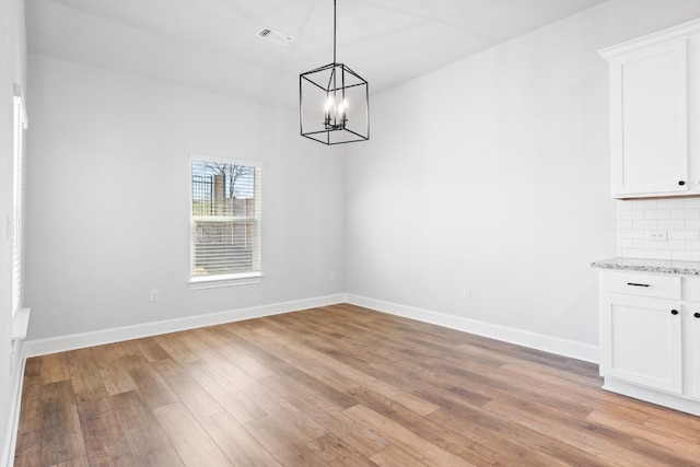 unfurnished dining area featuring an inviting chandelier and light hardwood / wood-style flooring