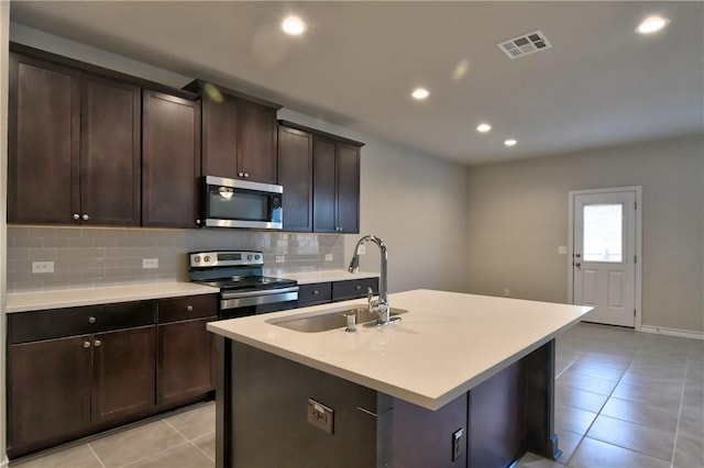 kitchen with dark brown cabinetry, appliances with stainless steel finishes, tasteful backsplash, sink, and a center island with sink