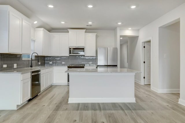 kitchen featuring appliances with stainless steel finishes, a center island, light stone countertops, and white cabinets