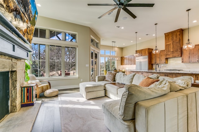 living room with ceiling fan, sink, and a stone fireplace