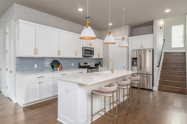 kitchen with white cabinetry, a center island with sink, appliances with stainless steel finishes, decorative light fixtures, and sink