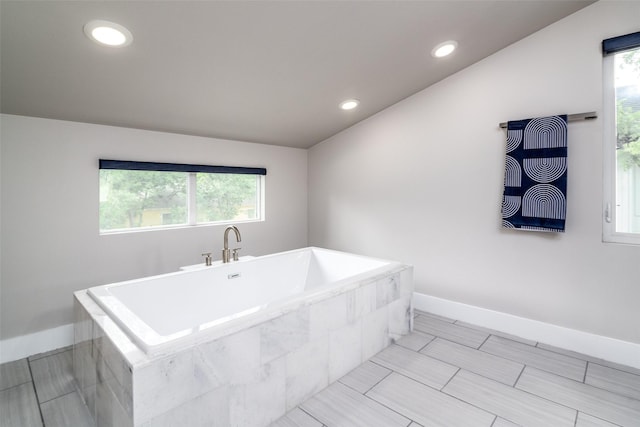 bathroom with vaulted ceiling, plenty of natural light, and tiled tub