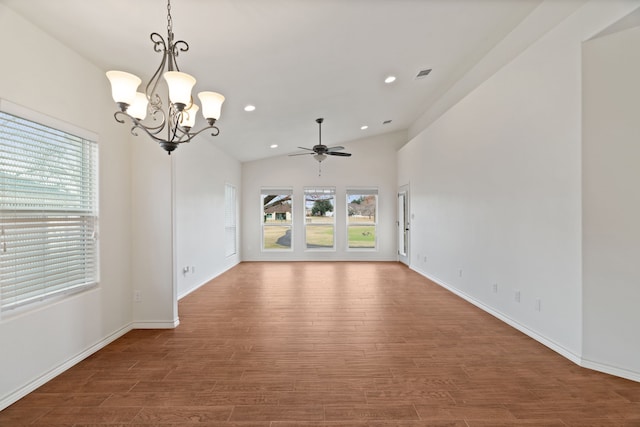 spare room with lofted ceiling, a wealth of natural light, ceiling fan with notable chandelier, and hardwood / wood-style floors