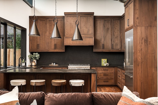 kitchen with decorative light fixtures, decorative backsplash, a kitchen bar, sink, and built in refrigerator