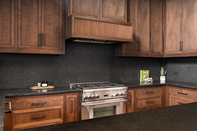 kitchen with wall chimney exhaust hood, backsplash, stainless steel range with gas cooktop, and dark stone counters