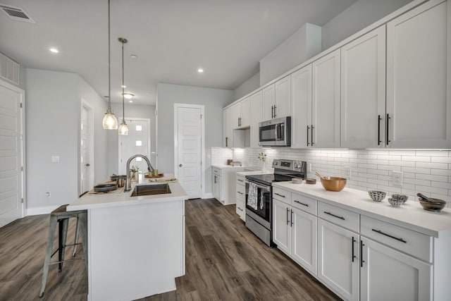 kitchen with hanging light fixtures, a kitchen island with sink, appliances with stainless steel finishes, and white cabinetry