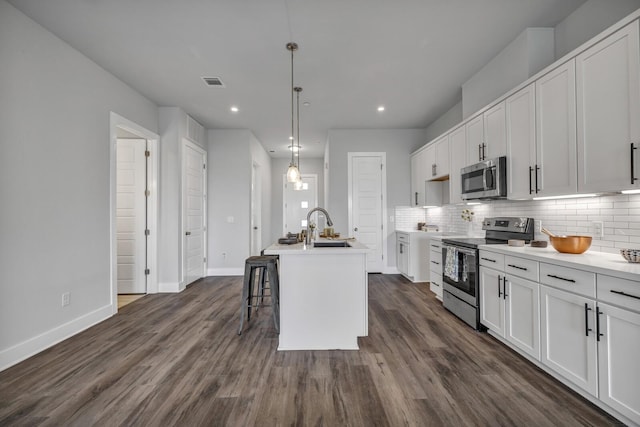 kitchen featuring white cabinets, decorative light fixtures, stainless steel appliances, a kitchen island with sink, and a breakfast bar area