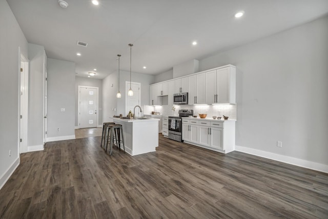 kitchen with pendant lighting, appliances with stainless steel finishes, white cabinetry, an island with sink, and a kitchen breakfast bar