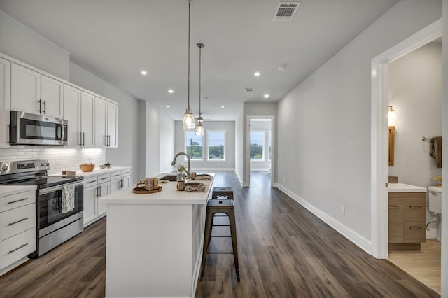 kitchen featuring dark hardwood / wood-style floors, pendant lighting, a kitchen island with sink, appliances with stainless steel finishes, and white cabinets