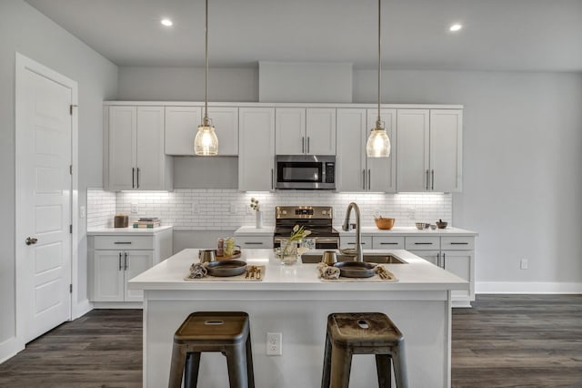 kitchen with hanging light fixtures, appliances with stainless steel finishes, and a kitchen island with sink