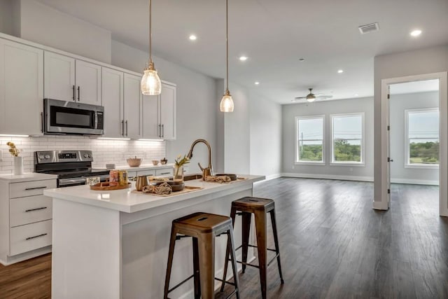 4507 E Martin Luther King Jr Blvd Unit 124, Austin, TX 78721 - kitchen with stainless steel appliances, decorative backsplash, dark wood finished floors, an island with sink, and a ceiling fan