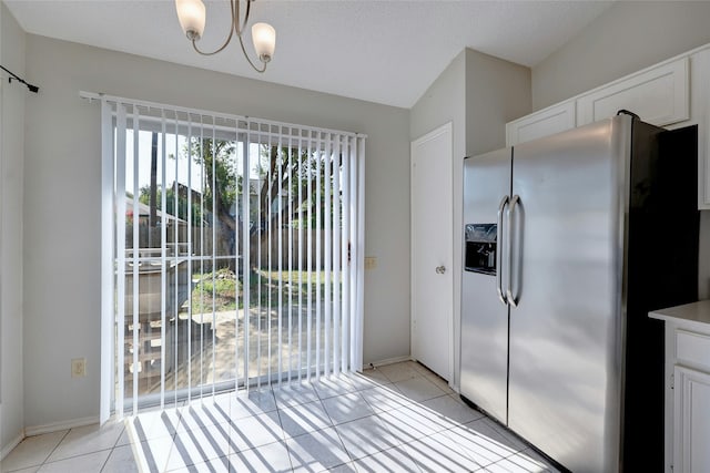 kitchen featuring pendant lighting, stainless steel refrigerator with ice dispenser, light tile patterned flooring, white cabinets, and a chandelier