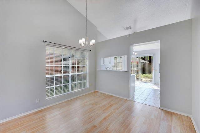 unfurnished dining area featuring a textured ceiling, vaulted ceiling, light hardwood / wood-style flooring, and an inviting chandelier