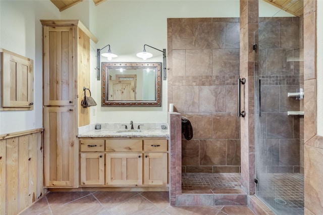 bathroom with wood walls, tiled shower, tile patterned flooring, lofted ceiling, and vanity