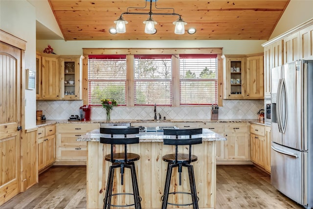 kitchen featuring vaulted ceiling, pendant lighting, a center island, a breakfast bar, and stainless steel fridge with ice dispenser