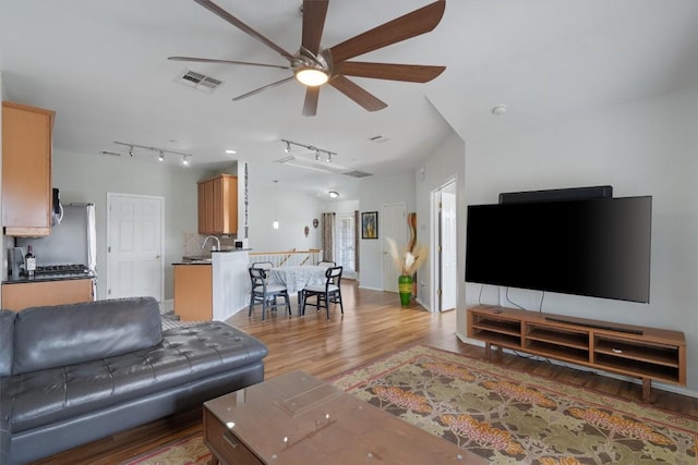 living room with visible vents, light wood-style flooring, ceiling fan, vaulted ceiling, and track lighting