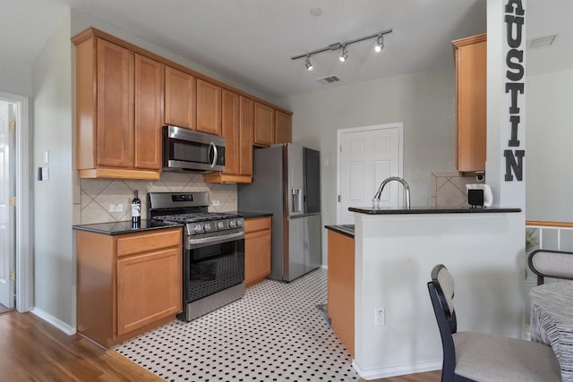 kitchen with appliances with stainless steel finishes, dark countertops, tasteful backsplash, and a peninsula