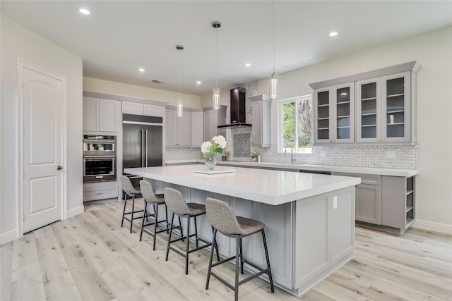 kitchen featuring stainless steel appliances, a spacious island, decorative light fixtures, wall chimney range hood, and a breakfast bar