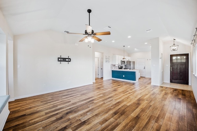 unfurnished living room featuring vaulted ceiling, ceiling fan with notable chandelier, and light hardwood / wood-style flooring