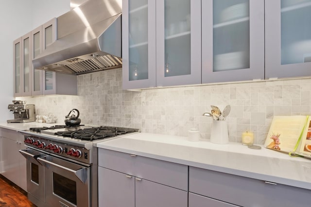 kitchen featuring gray cabinets, range with two ovens, backsplash, and wall chimney range hood