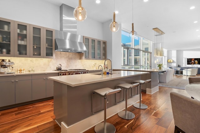 kitchen with decorative light fixtures, dark wood-type flooring, a kitchen island with sink, and range hood