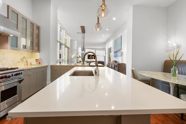 kitchen with decorative light fixtures, a large island with sink, gray cabinets, high end stainless steel range oven, and wall chimney exhaust hood