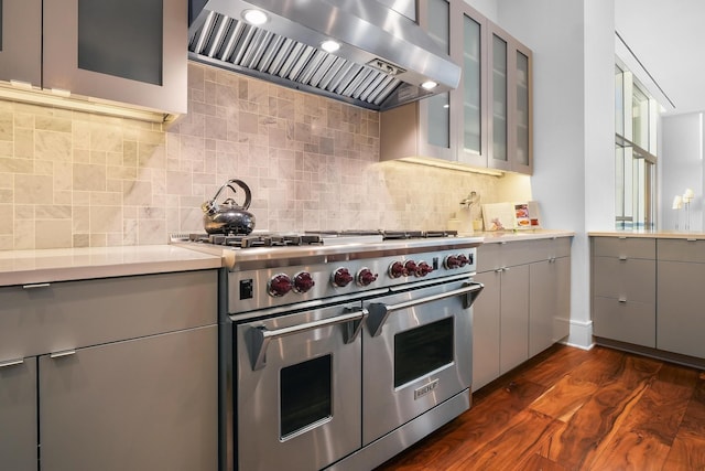 kitchen featuring exhaust hood, double oven range, decorative backsplash, gray cabinetry, and dark hardwood / wood-style floors