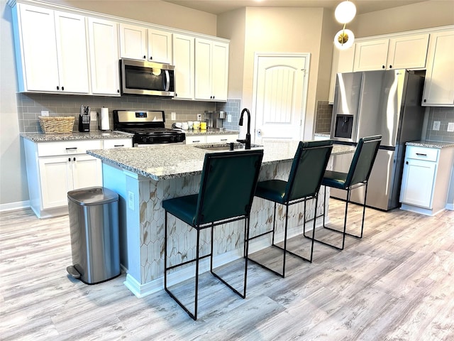 kitchen with white cabinetry, appliances with stainless steel finishes, a kitchen island with sink, light stone counters, and sink