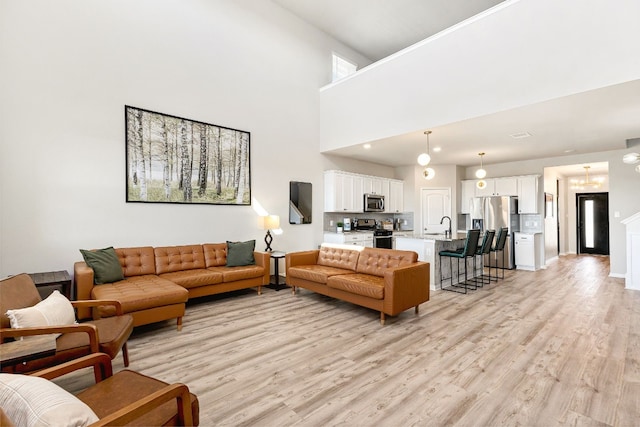 living room featuring a high ceiling, sink, and light hardwood / wood-style flooring