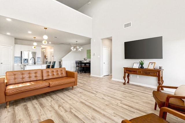 living room featuring a towering ceiling, a chandelier, and light wood-type flooring