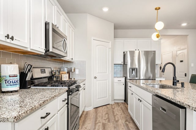 kitchen featuring decorative light fixtures, sink, white cabinets, light stone counters, and stainless steel appliances