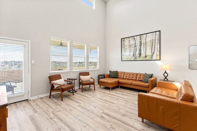 living room featuring a towering ceiling, light hardwood / wood-style flooring, and a healthy amount of sunlight